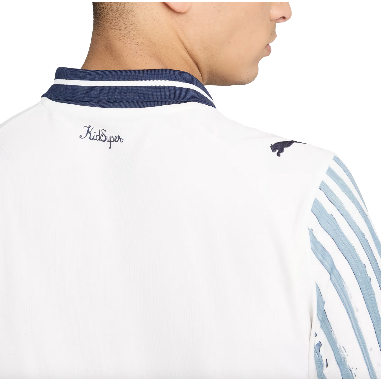 Close-up back view of a white Puma x KidSuper shirt with a navy striped collar, "KidSuper" script logo, and a Puma logo on the shoulder.