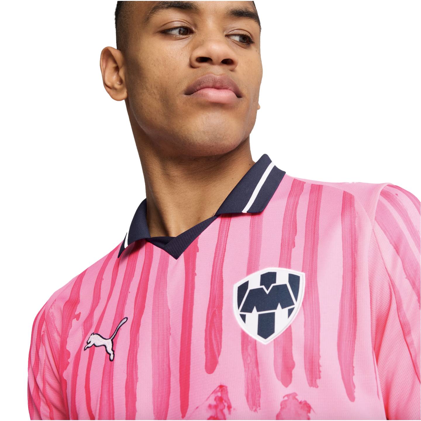 A man wearing a pink C.F. Monterrey soccer jersey with dark pink stripes, a navy collar, and the team crest, looking to the side against a white background.