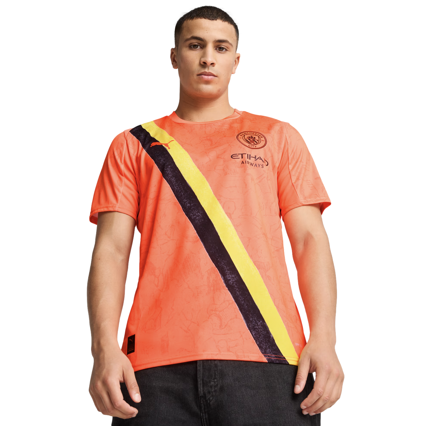 A young man wearing an orange Manchester City football jersey with a black and yellow diagonal sash.