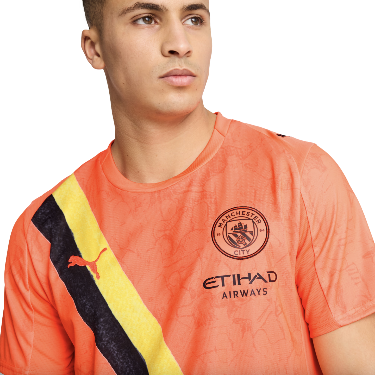 A man wearing an orange Manchester City soccer jersey featuring a diagonal black and yellow sash, the club crest, and the Etihad Airways sponsor logo.