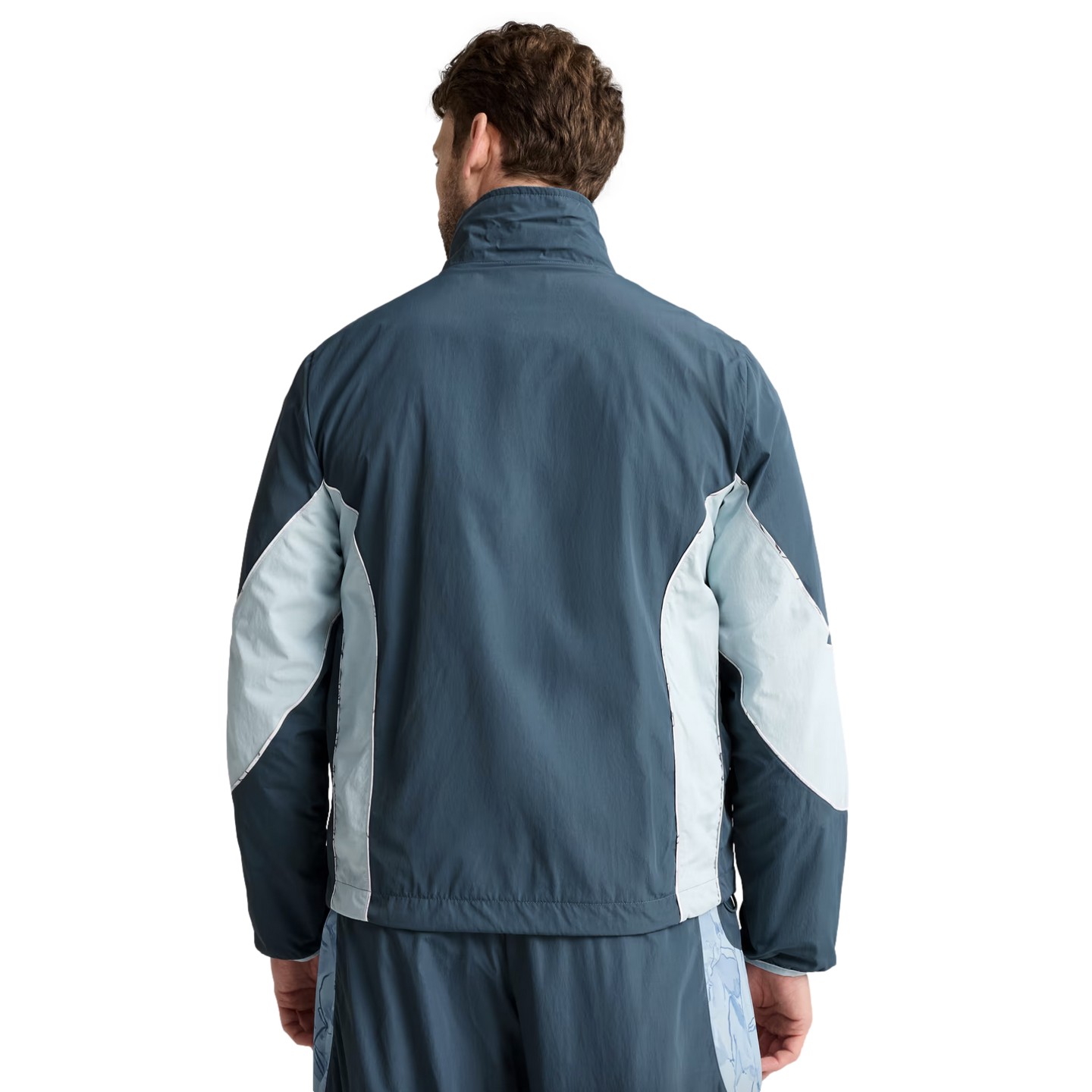Back view of a man wearing a blue and light blue paneled athletic jacket and matching shorts.