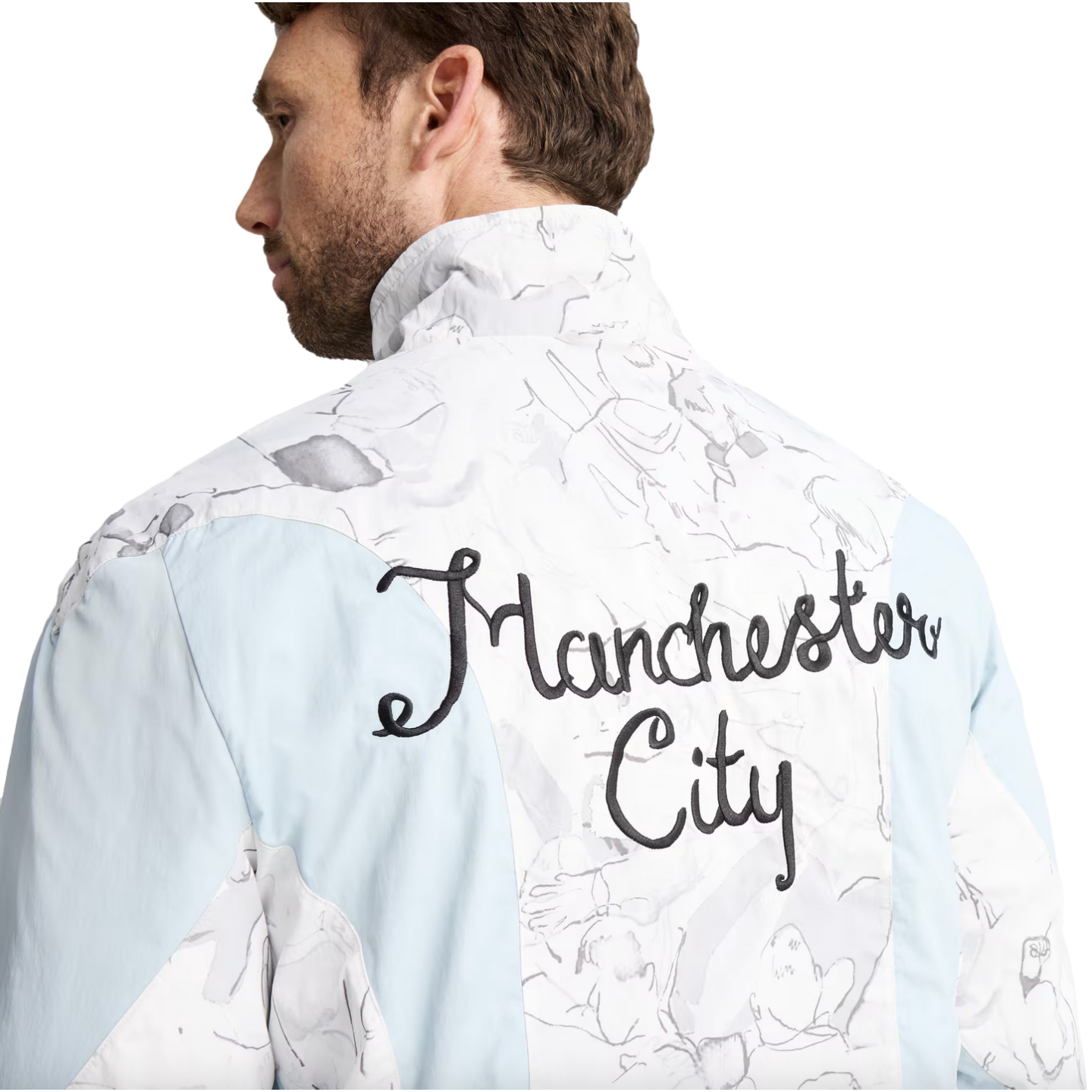 Rear view of a man in a light blue and white marbled jacket with "Manchester City" embroidered in black cursive script on the back.