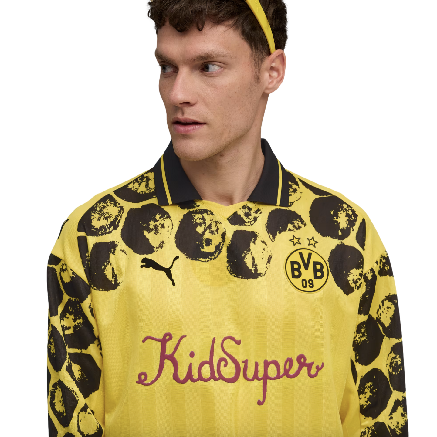 A man wearing a yellow and black KidSuper x Puma BVB long-sleeve jersey with a spotted pattern on the sleeves and shoulders against a white background.