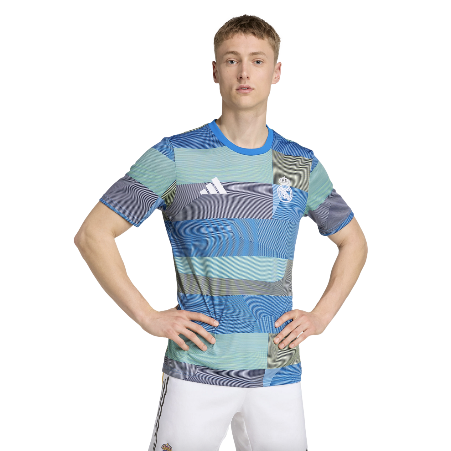 A man wearing a blue and green patterned Real Madrid football shirt and white shorts stands with his hands on his hips against a white background.