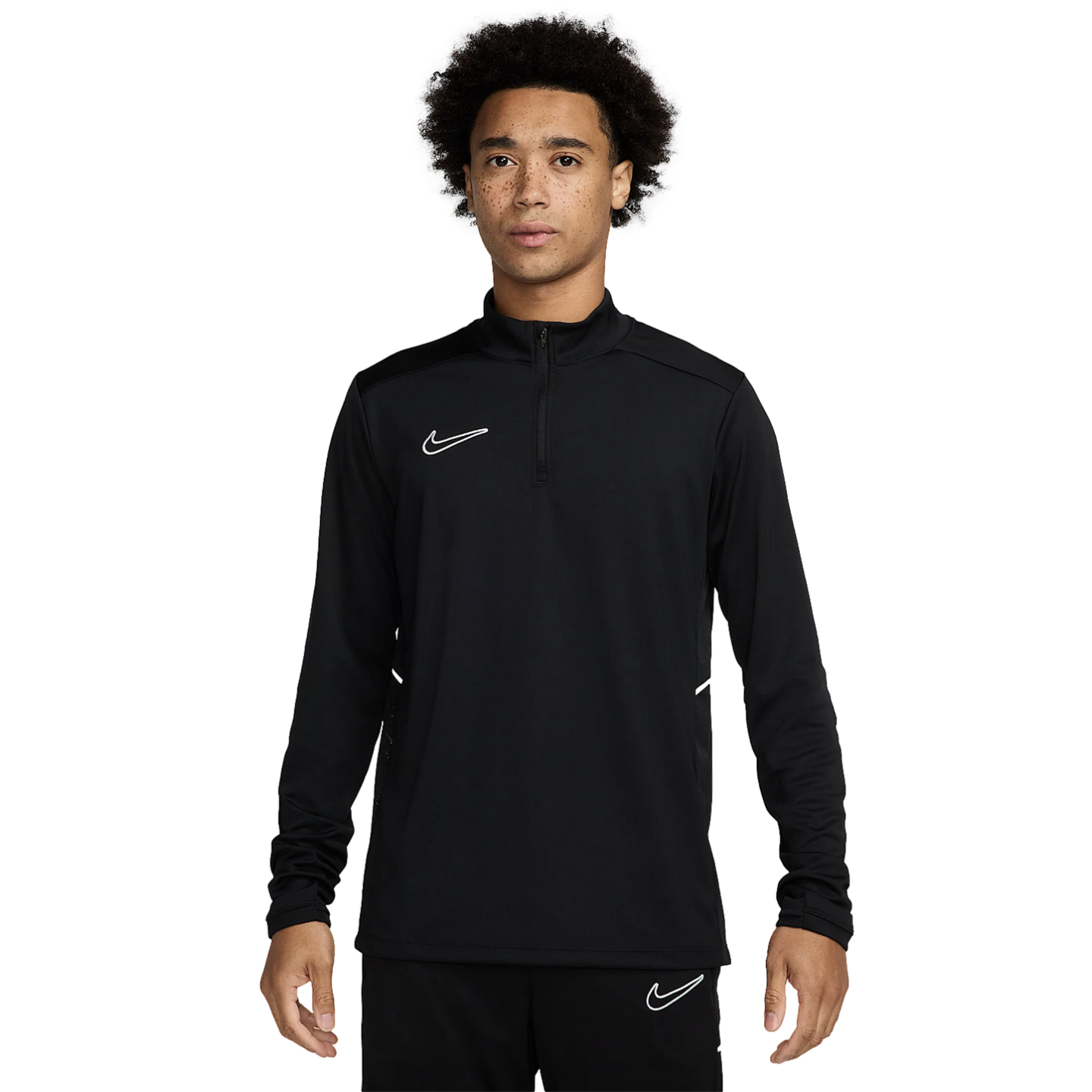 A young man with curly hair and freckles wearing a black Nike quarter-zip long-sleeve athletic top and matching black pants, standing against a white background.
