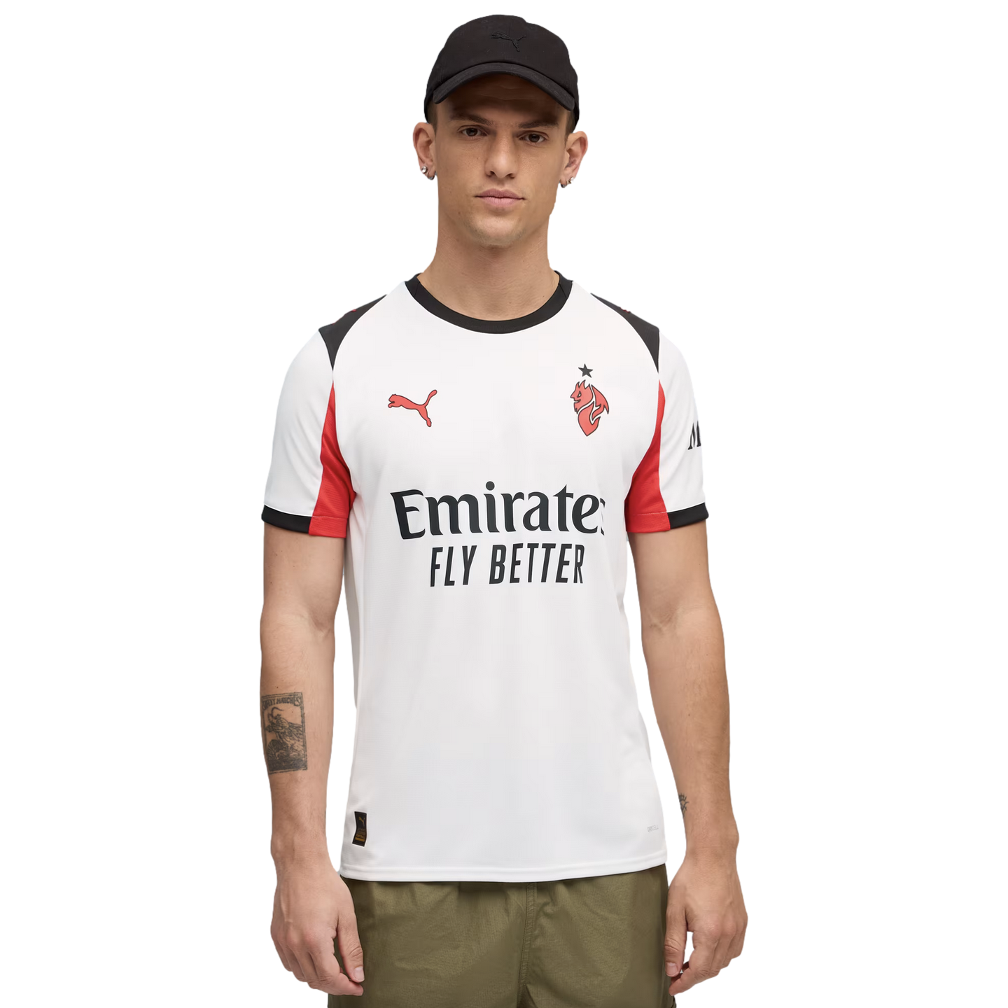 A man wearing a white Puma AC Milan soccer jersey with red accents, a black cap, and olive green pants against a black background.