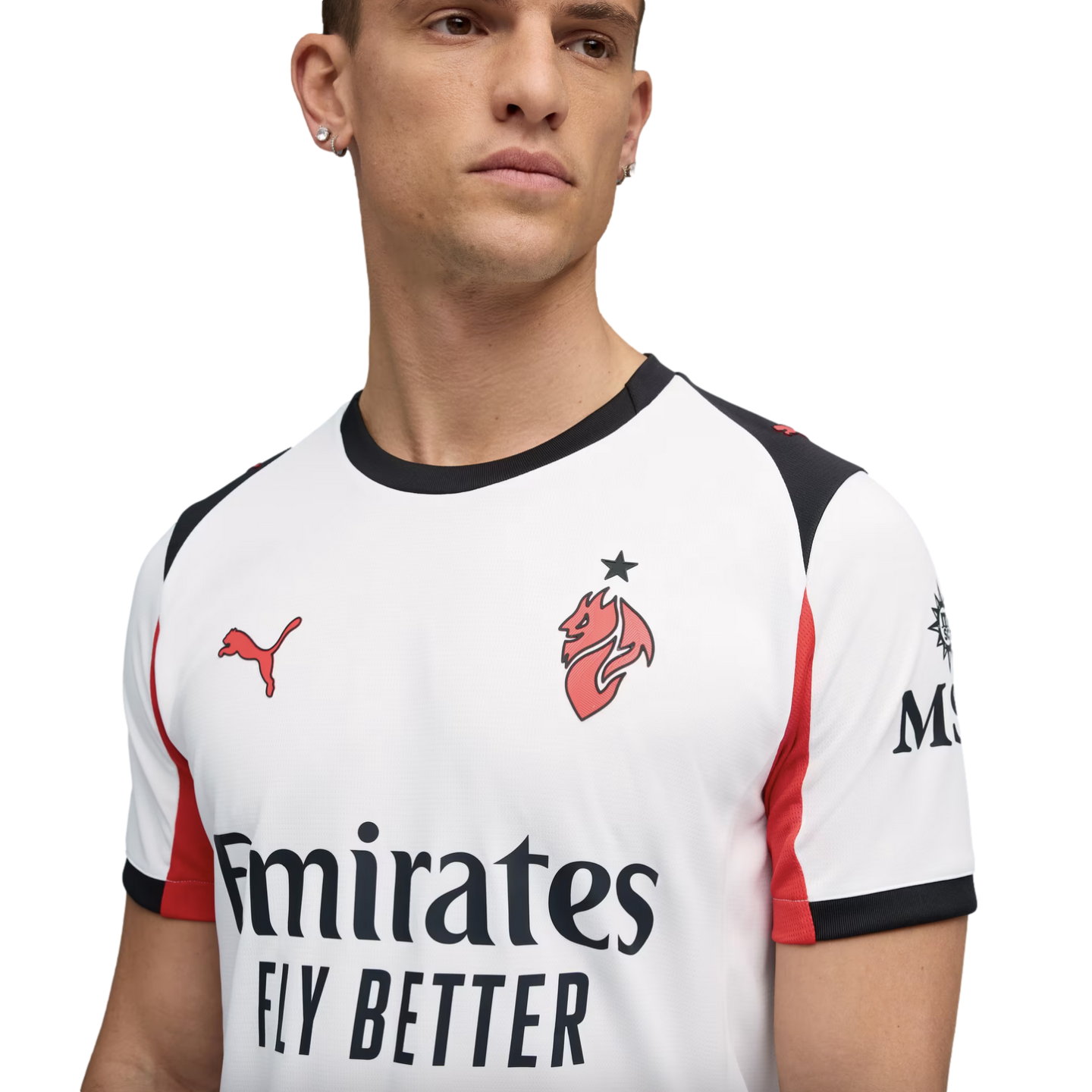 A man models a white AC Milan football jersey by Puma, featuring red and black accents and the "Emirates FLY BETTER" sponsor logo, against a solid black background.
