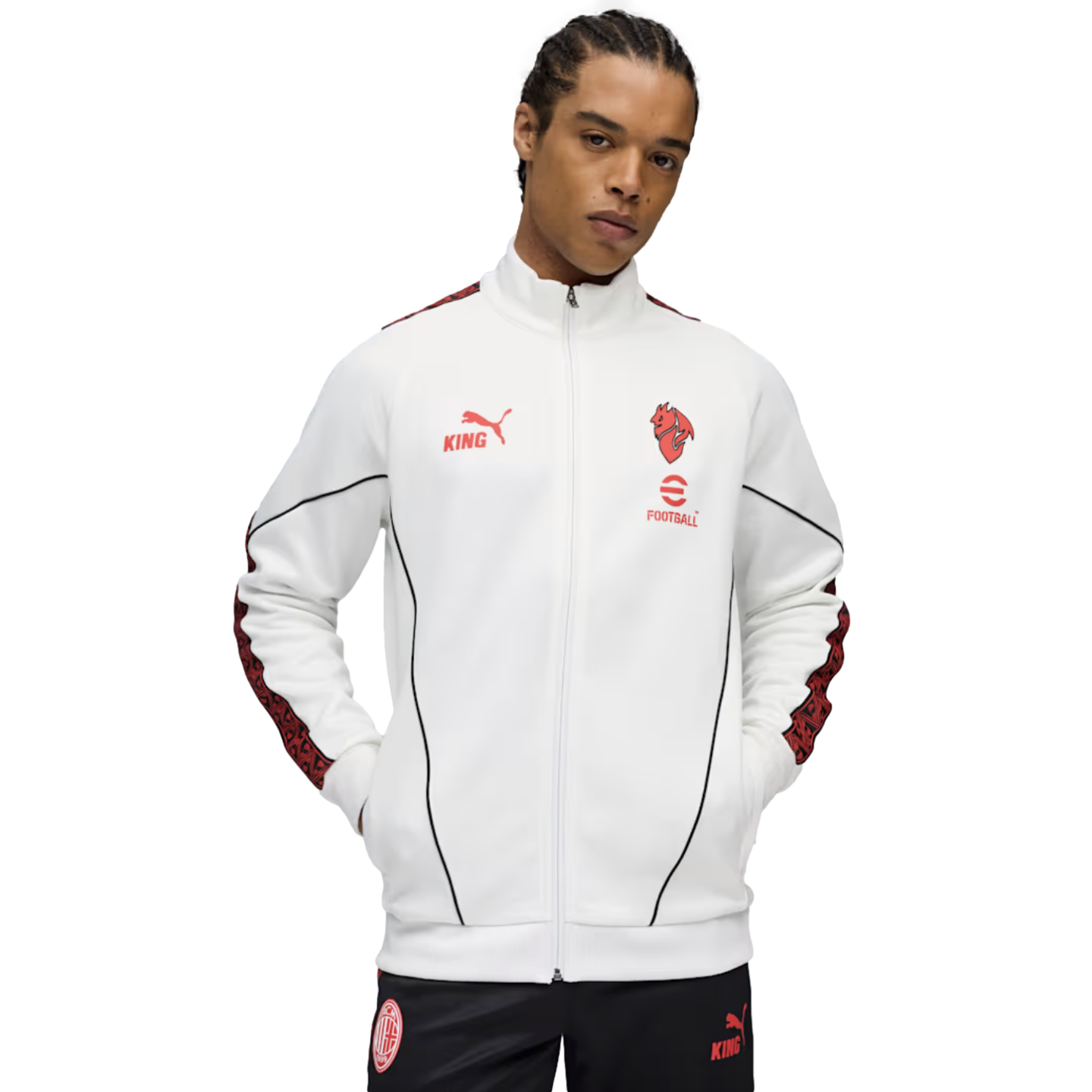 A man wearing a white Puma KING track jacket with red accents and black AC Milan pants against a black background.