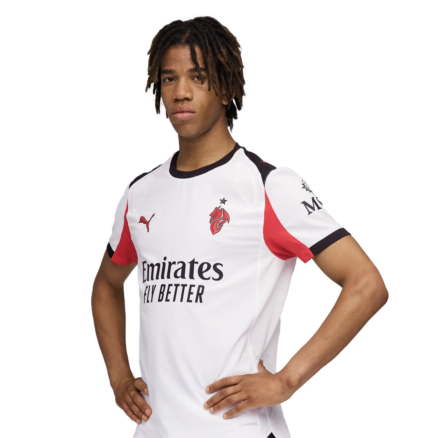 A young soccer player with dreadlocks wears a white AC Milan jersey, posing with hands on his hips against a solid black background.