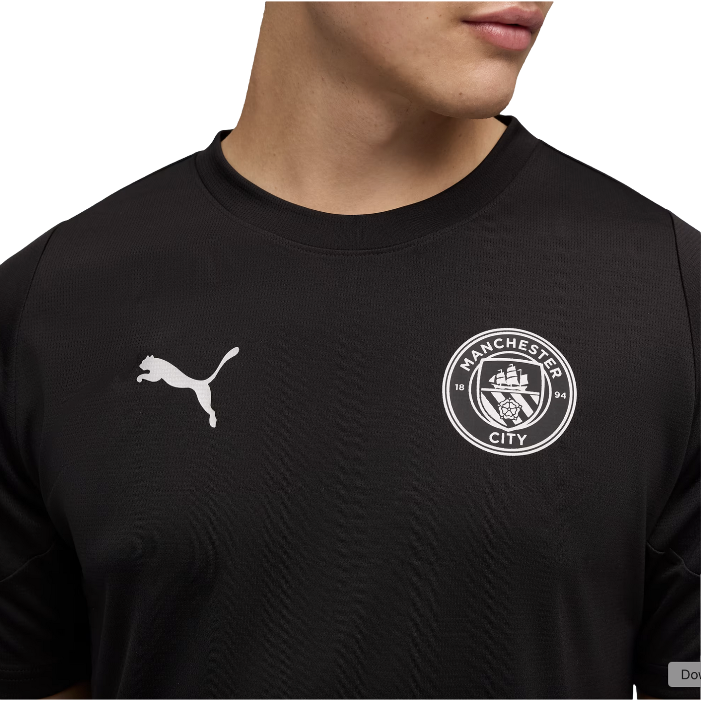 A person wearing a black Manchester City football shirt with a white Puma logo and the club's monochrome crest on the chest.