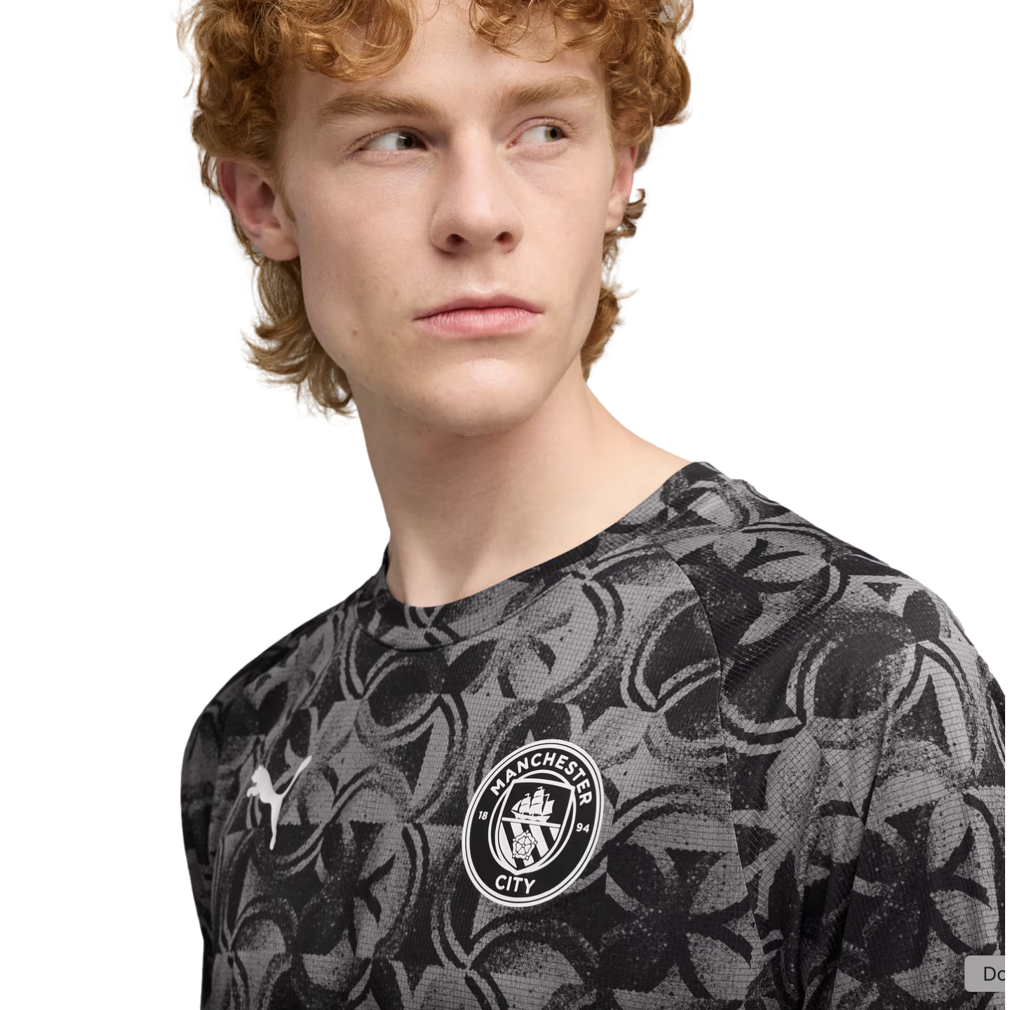 Man with red curly hair wearing a grey and black patterned Manchester City Puma jersey, looking off-camera against a black background.