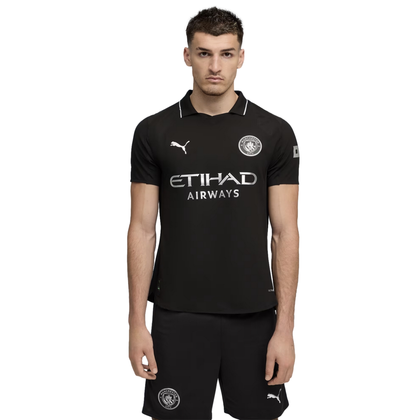 A man wearing a black Manchester City soccer kit with silver logos and sponsors, set against a solid black background.