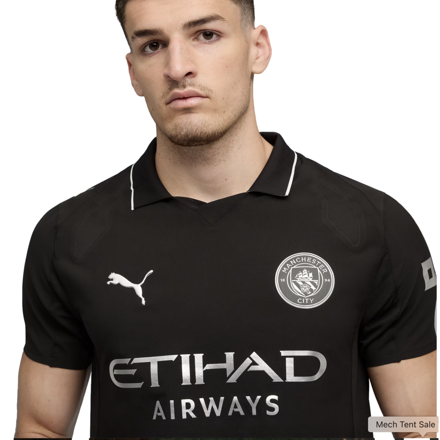 A young man wearing a black Manchester City soccer jersey with silver club crest, Puma, and Etihad Airways logos.