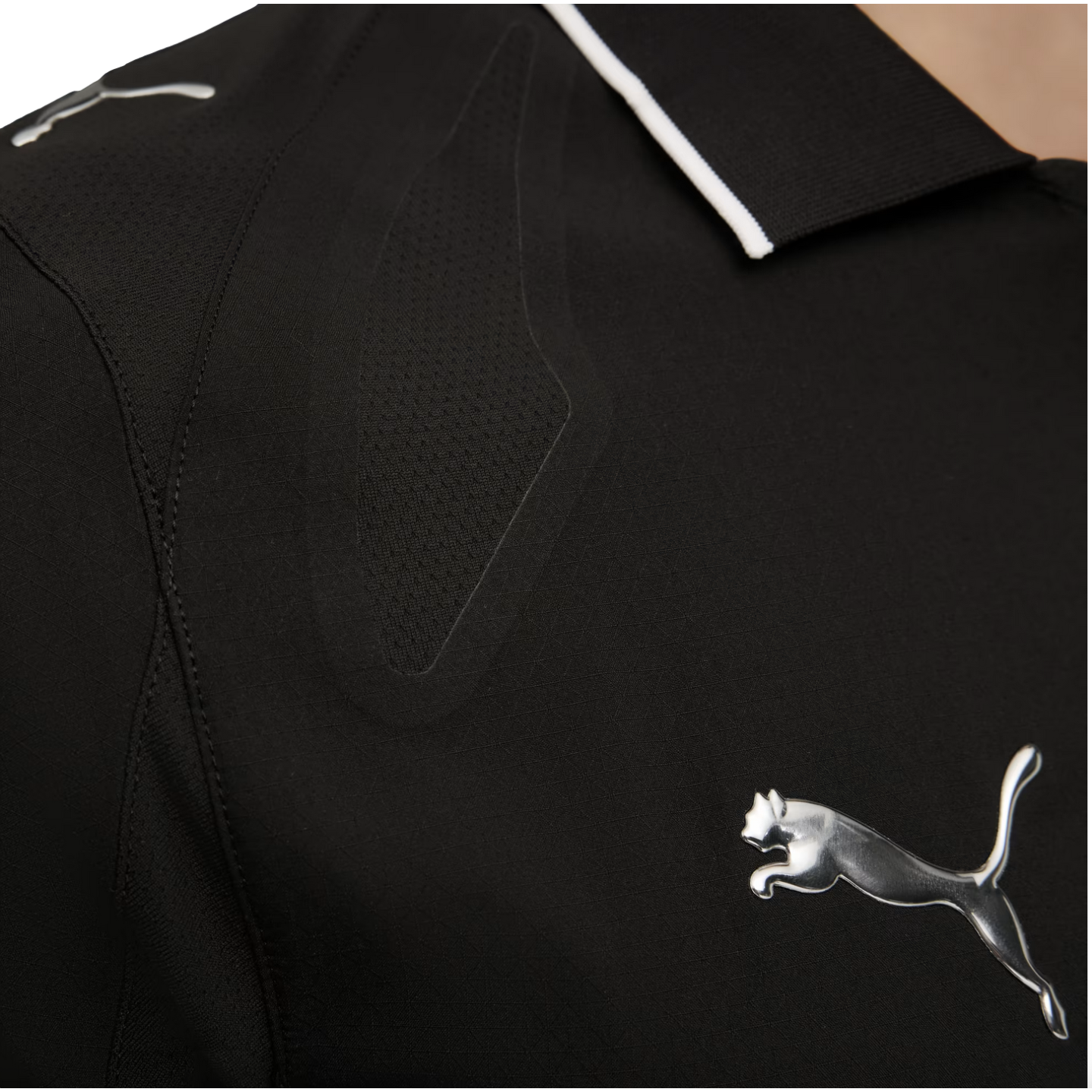 Close-up of black athletic wear with a metallic silver Puma logo. The garment features a textured mesh panel and a black collar with thin white trim.
