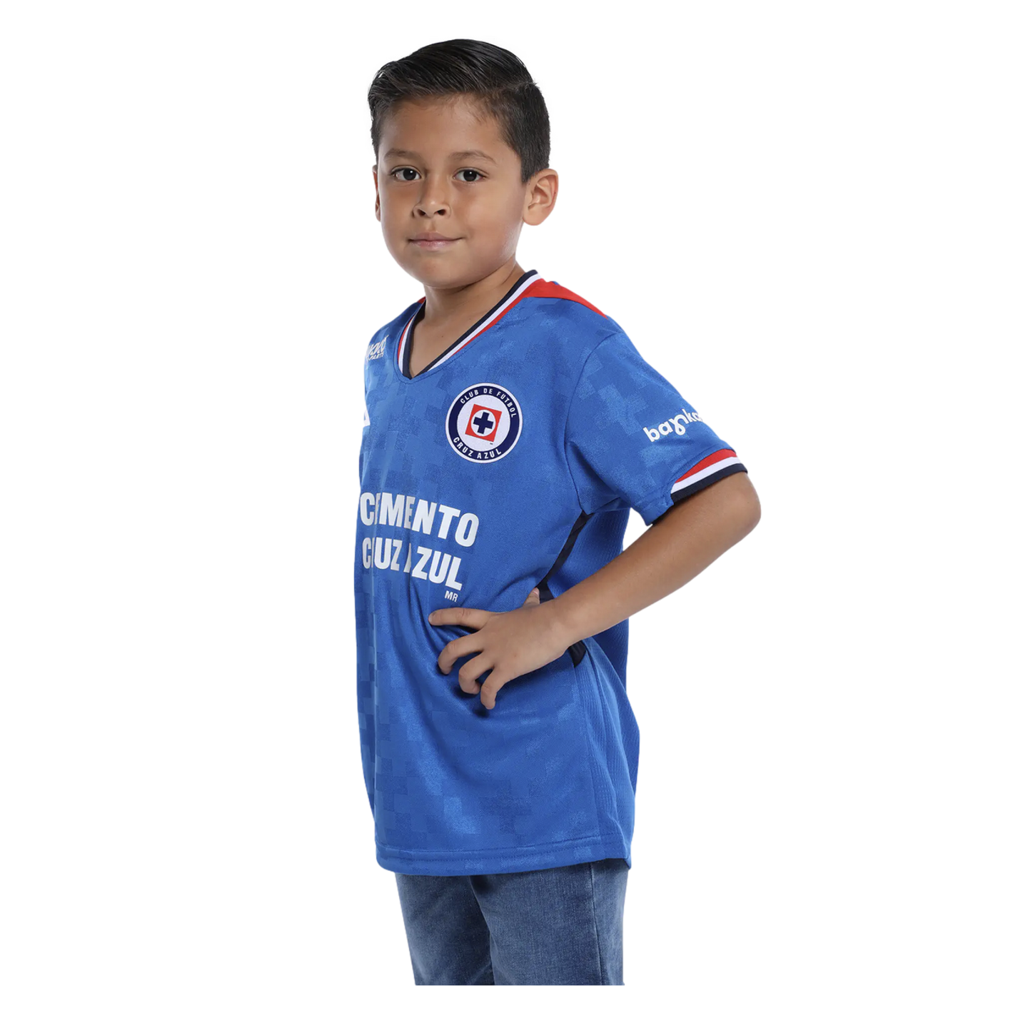 A young boy posing in a blue Cruz Azul soccer jersey and jeans against a solid black background.