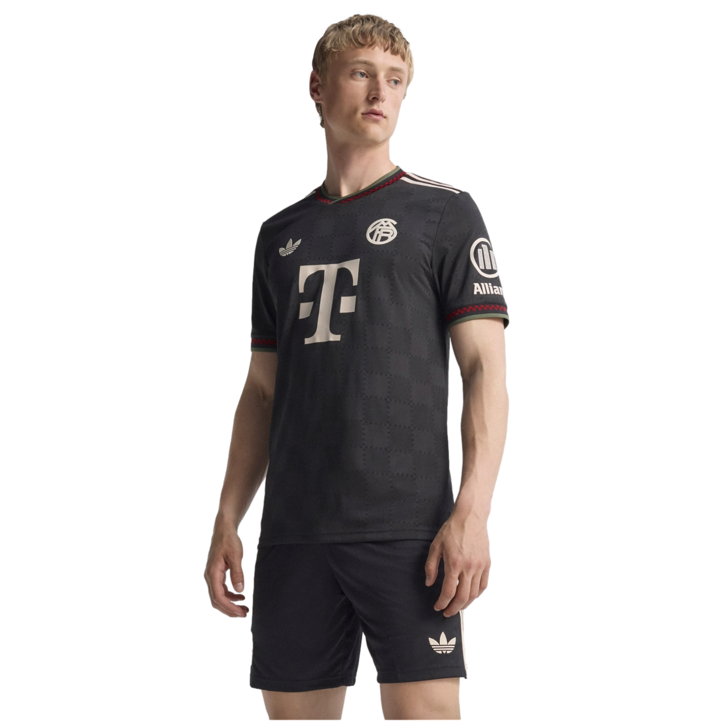 A man models a black Bayern Munich soccer kit with a large "T" logo and Adidas trefoil logo against a black background.