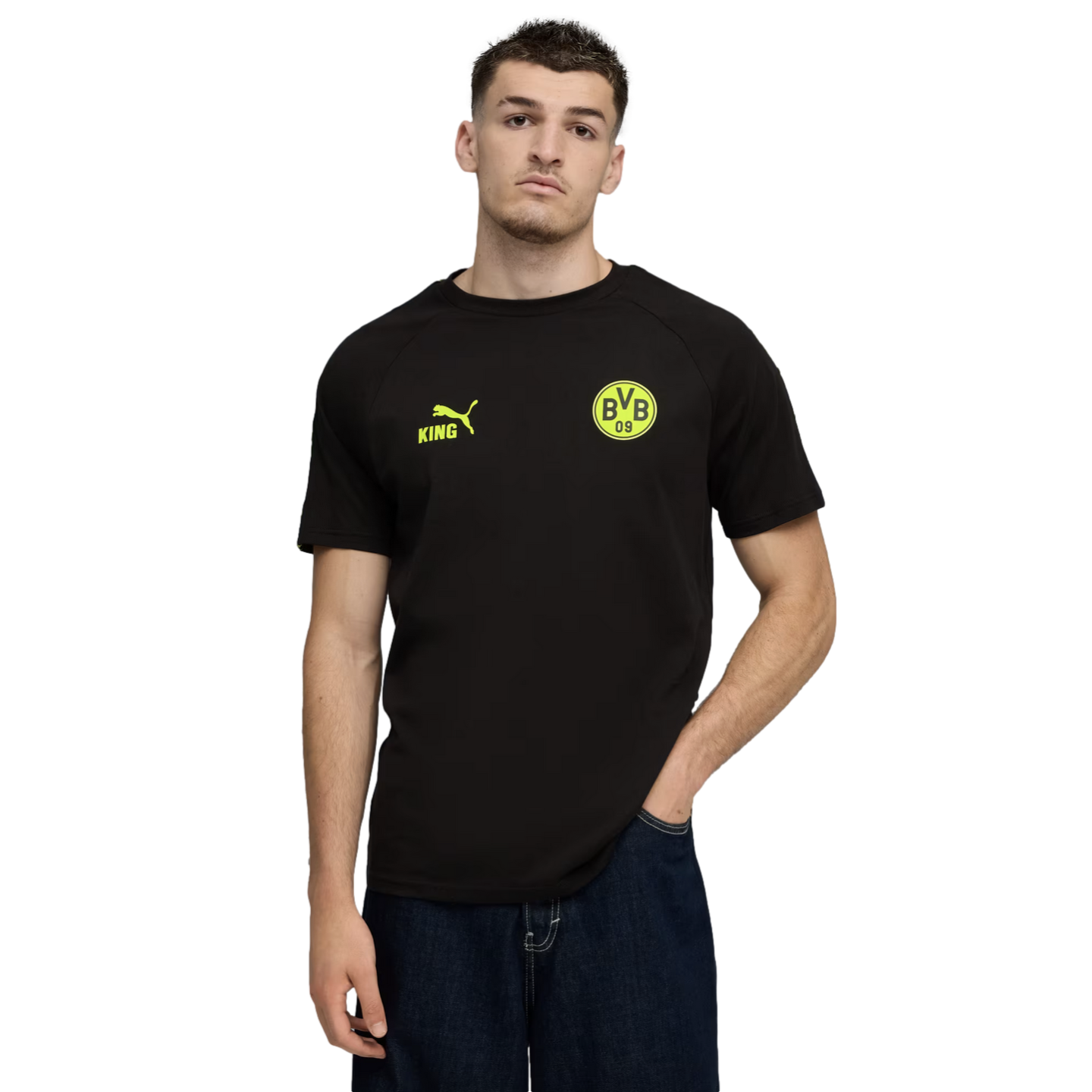 A man in a black T-shirt with yellow Puma King and BVB 09 logos and dark blue jeans, posing against a plain black background.