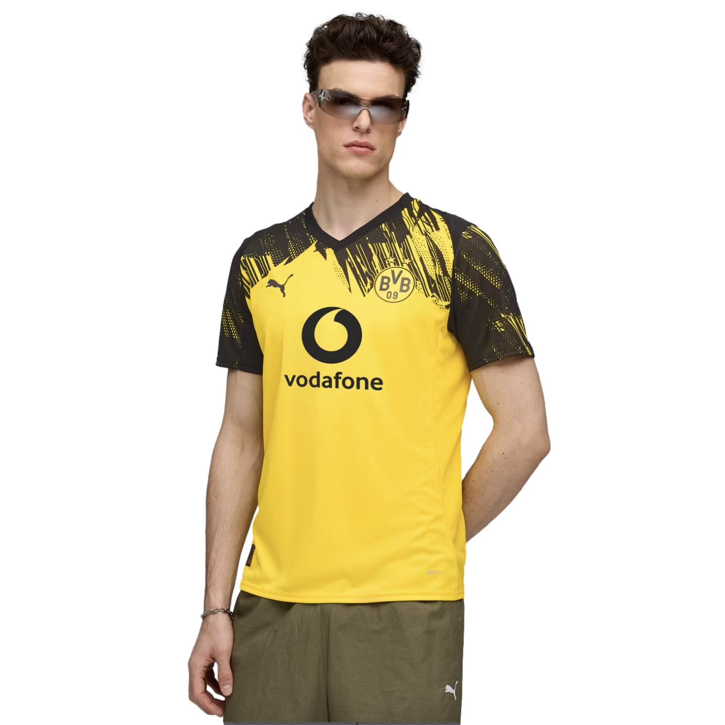 A man wearing a yellow and black Borussia Dortmund soccer jersey with a Vodafone logo, sunglasses, and olive shorts.