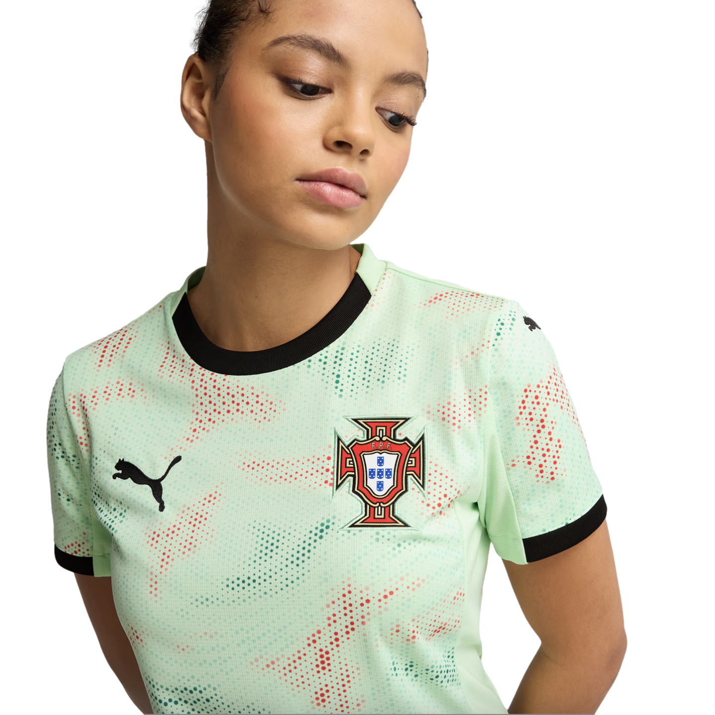 Young woman wearing a mint-green Puma Portugal soccer jersey with black trim and a red and green dotted pattern, looking down against a black background.