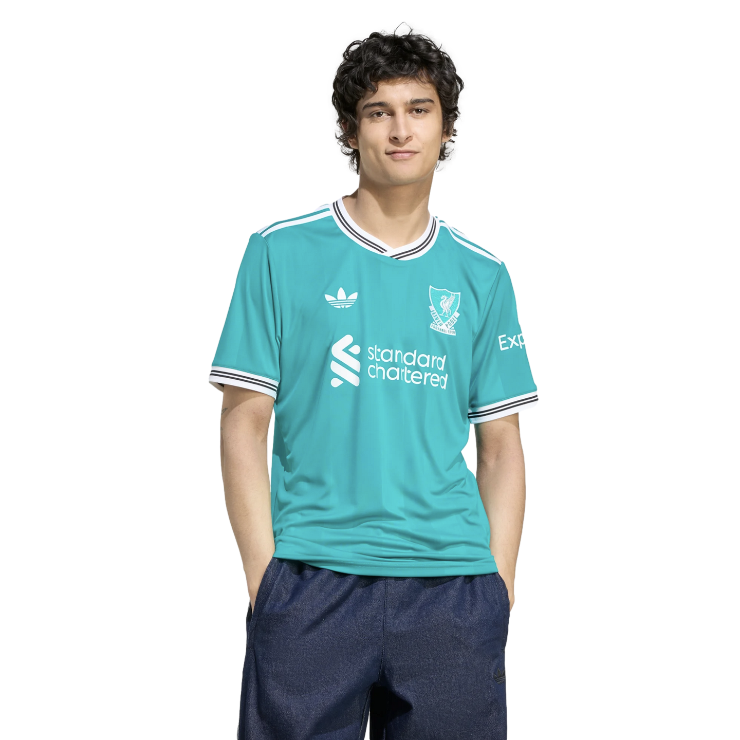 A man wearing a turquoise Liverpool FC jersey and dark blue shorts, standing against a black background.
