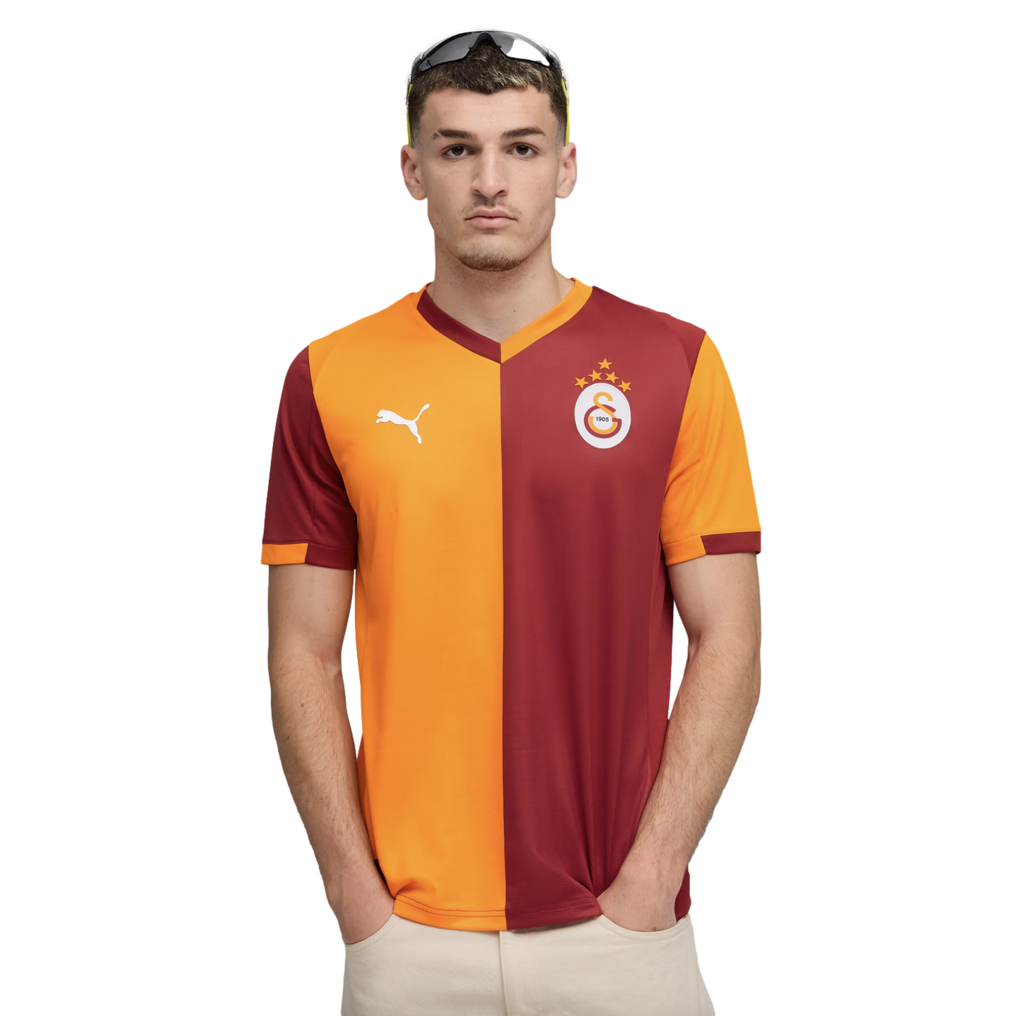 Man in an orange and maroon Galatasaray football jersey with a white Puma logo and team crest, standing against a black background with hands in pockets.