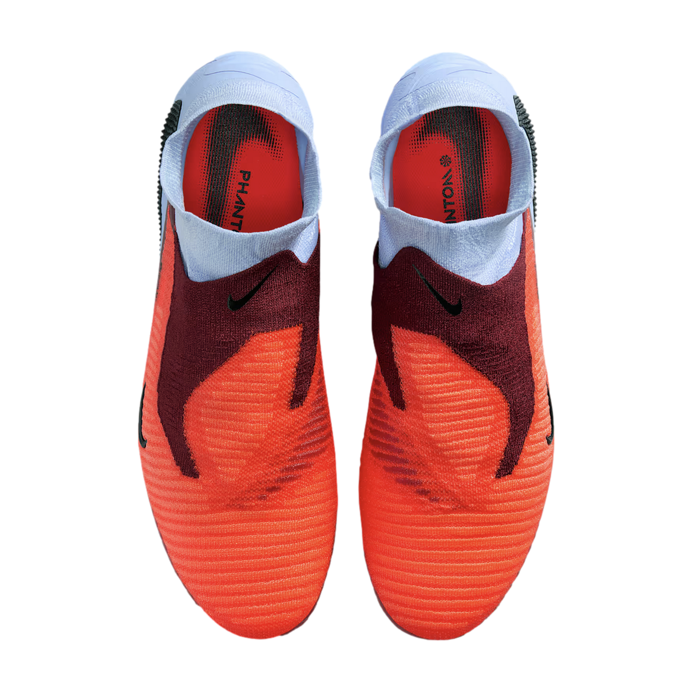 Top-down view of a pair of laceless Nike Phantom football boots in bright orange, maroon, and light blue against a black background.