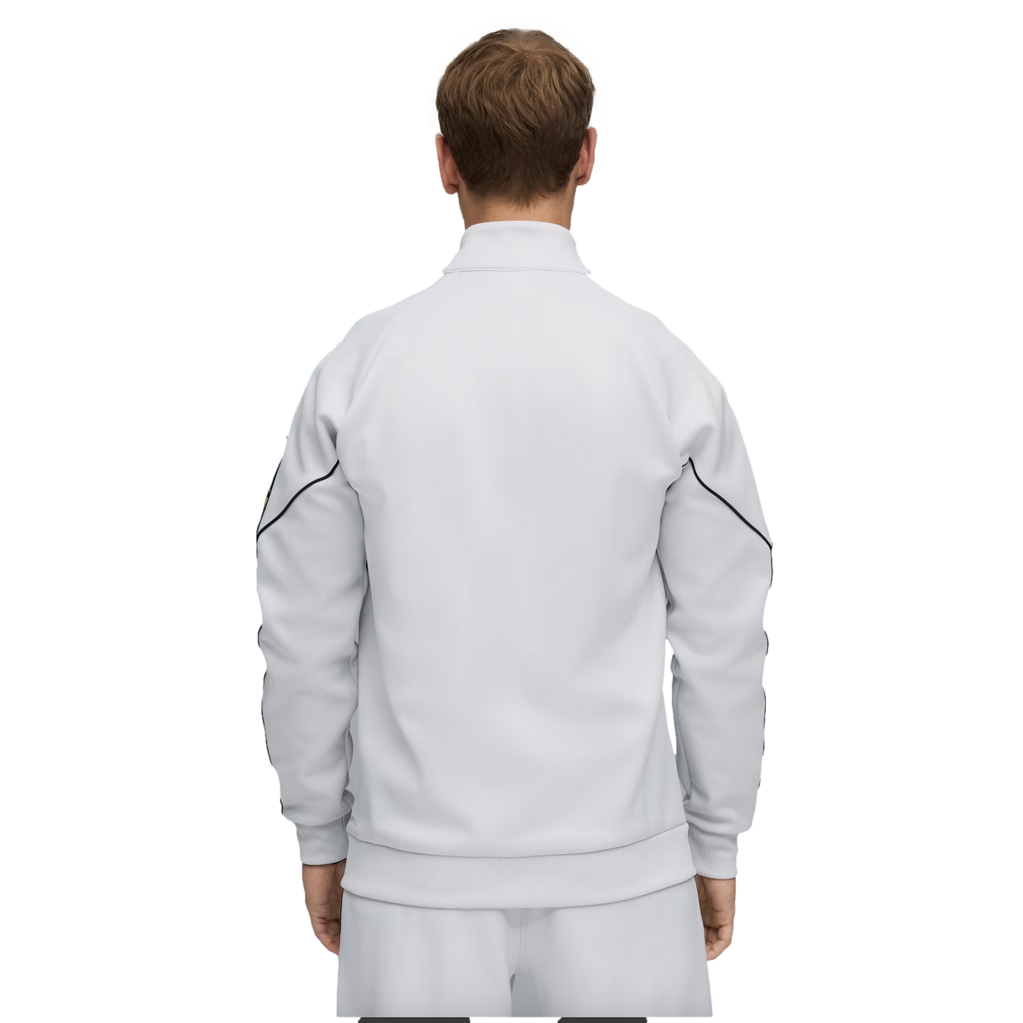 Back view of a person in a white track jacket with black sleeve piping and matching pants, standing against a solid black background.