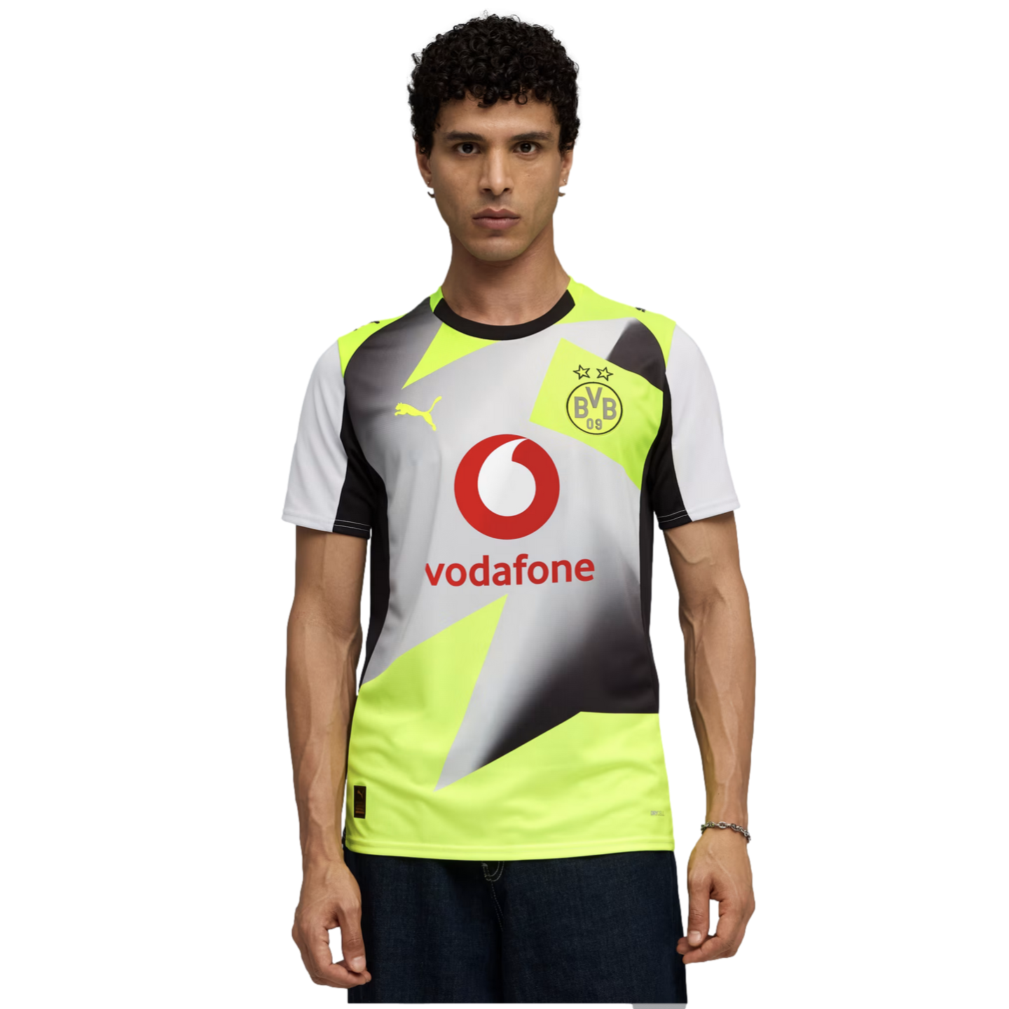 Man with curly hair wearing a yellow and grey geometric Puma BVB soccer jersey with a red Vodafone logo, set against a solid black background.