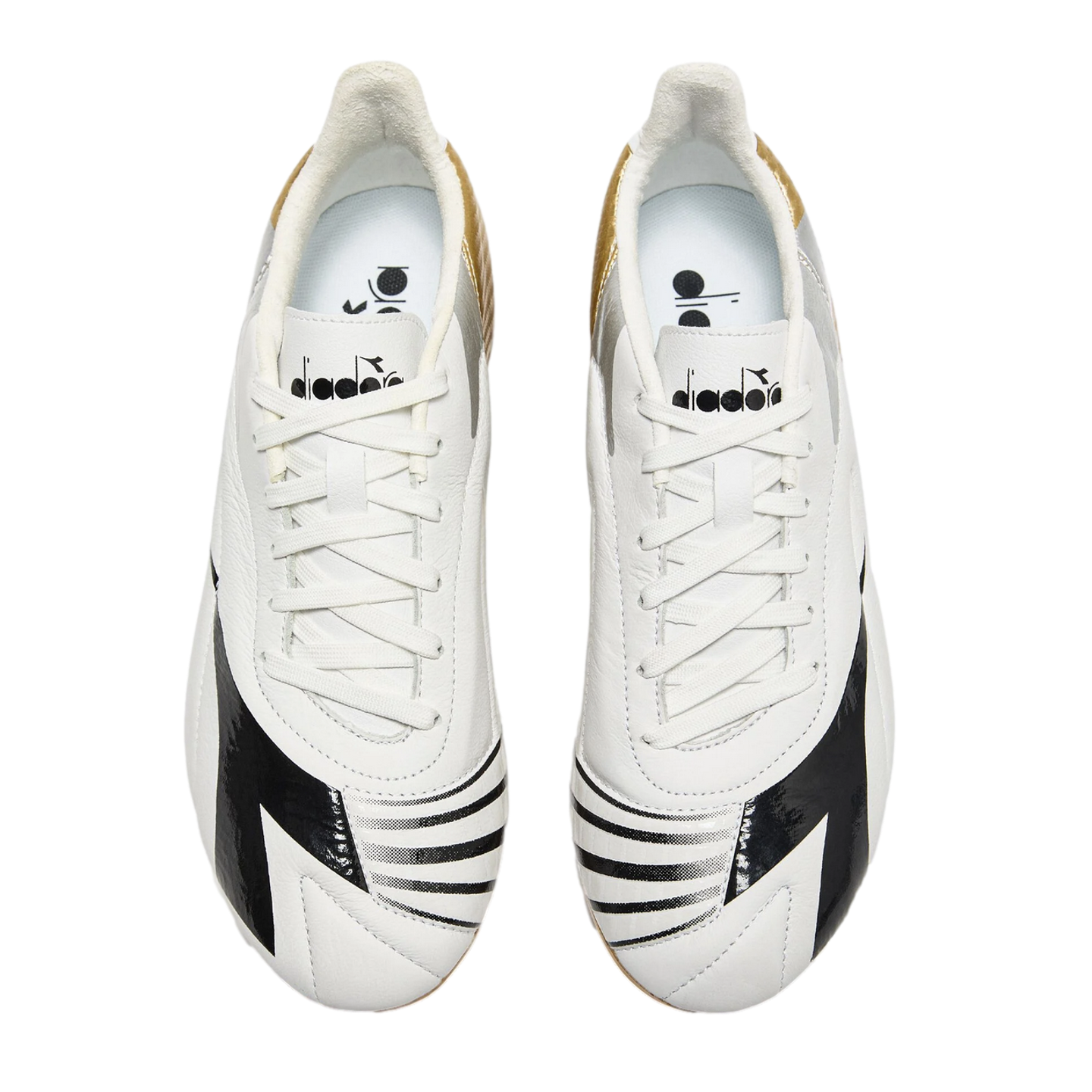 Top-down view of white Diadora soccer cleats with black graphic patterns on the toes and gold and silver accents on the heels, against a black background.