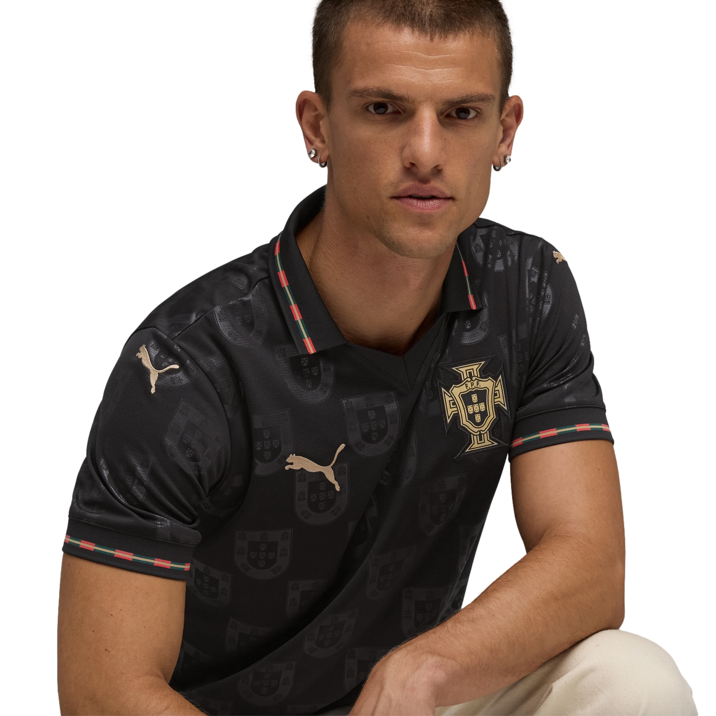 Man wearing a patterned black Puma Portugal jersey with gold logos and red-green striped trim, against a black background.