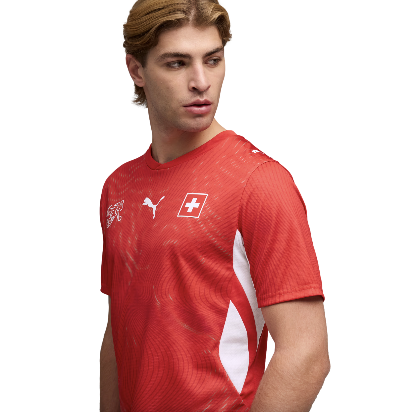 A man in a red Puma Switzerland national soccer jersey, looking to the side against a black background.