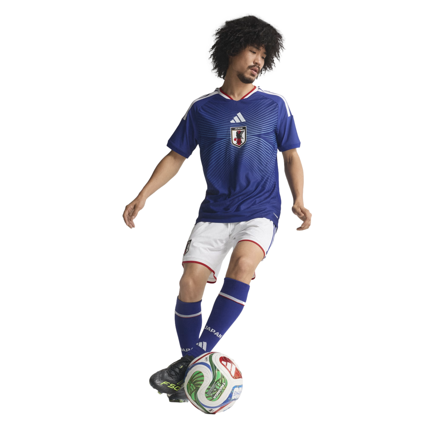 A soccer player with an afro, wearing a blue Japan national team jersey and white shorts, dribbles a soccer ball against a solid black background.