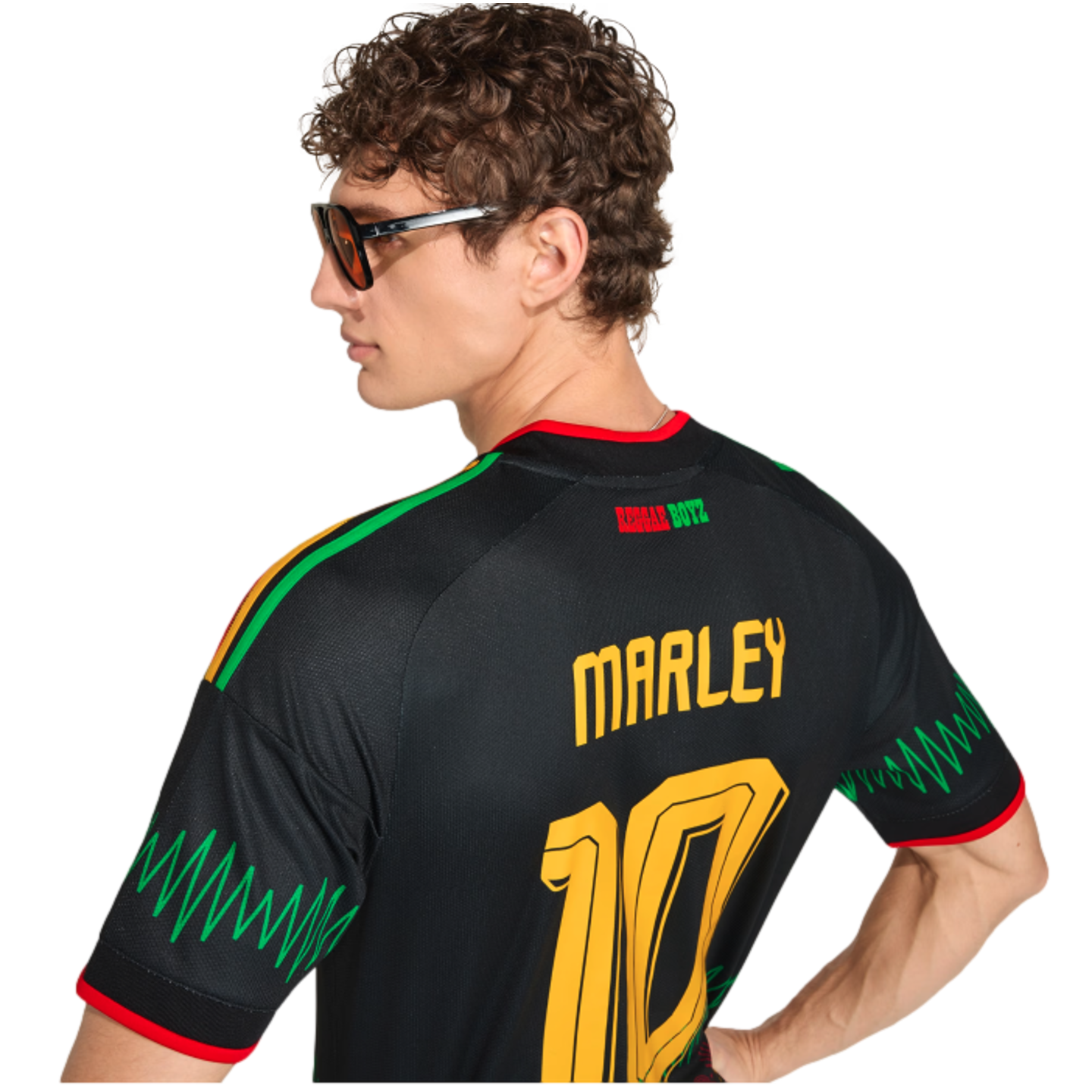 A man in sunglasses seen from behind, wearing a black "MARLEY 10" Reggae Boyz jersey with green zigzag patterns on the sleeves.
