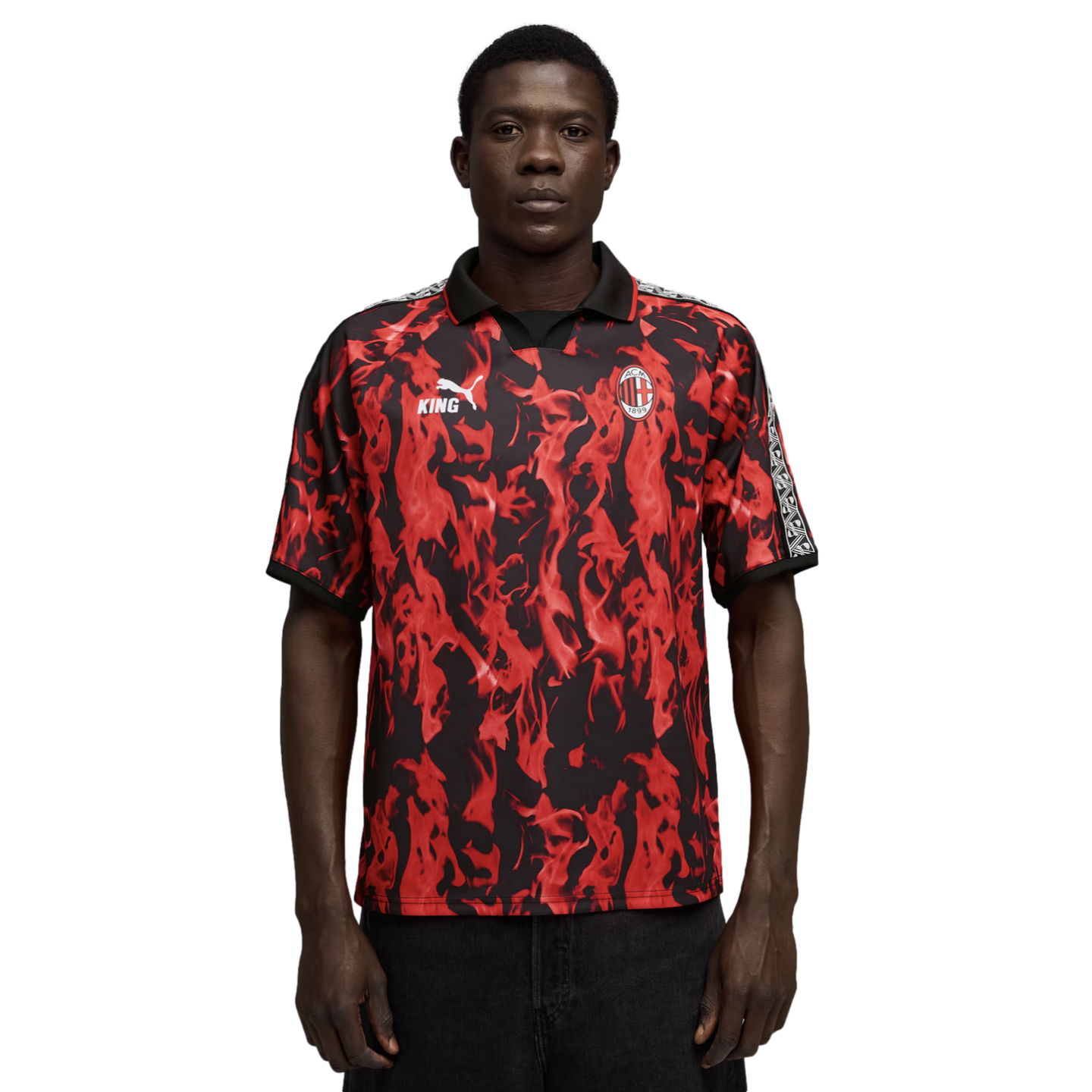 Man in a red and black flame-patterned AC Milan soccer jersey with a black collar, standing against a black background.
