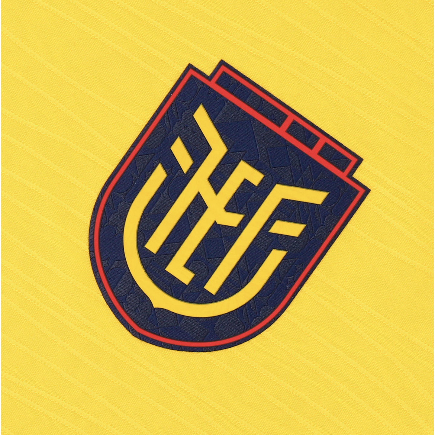 A close-up of a navy blue and yellow crest with stylized letters "FEF" centered on a bright yellow, textured fabric background. The crest has a thin red border and a subtle geometric pattern within the blue field.