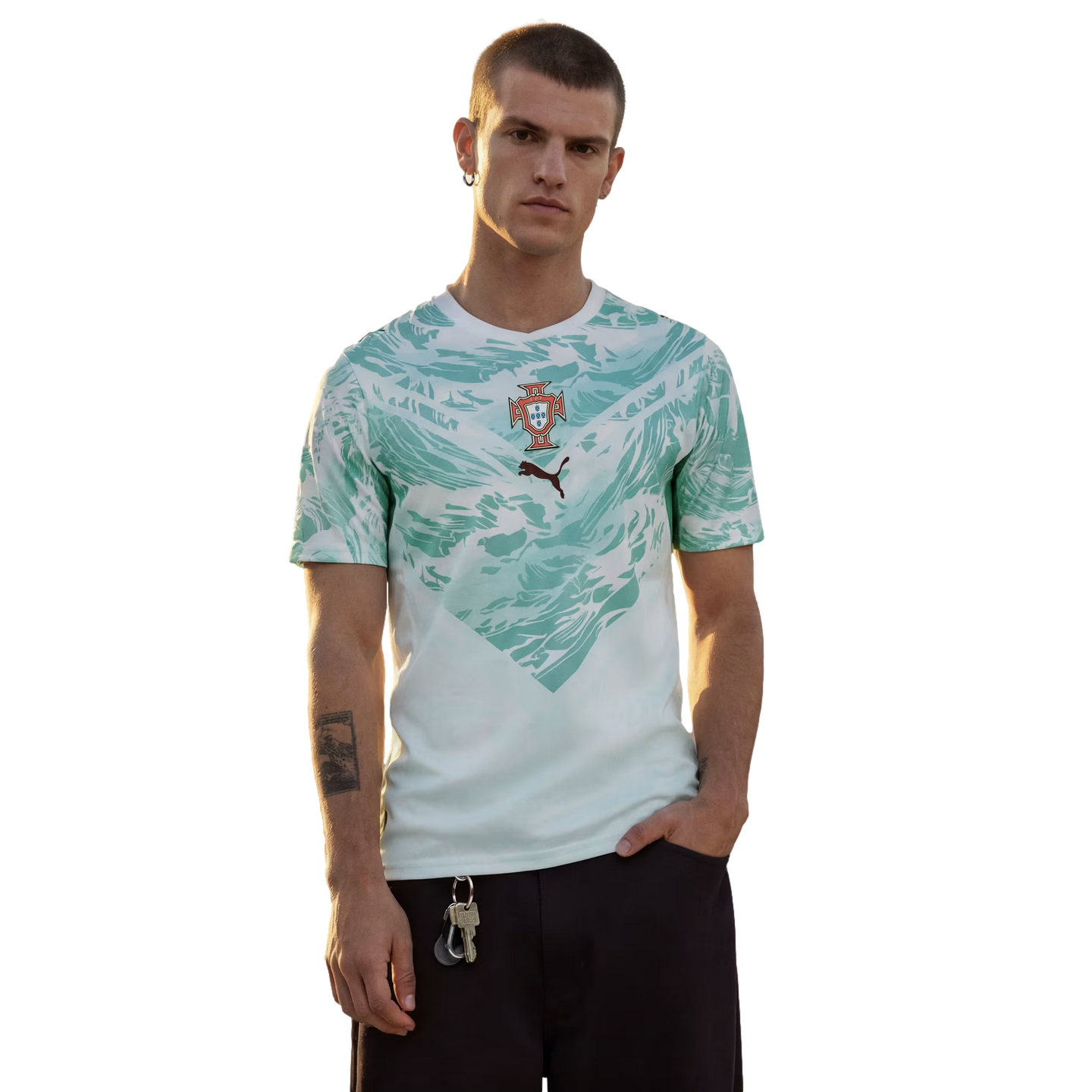 A man stands against a black background wearing a white t-shirt with a light teal abstract pattern, the Portugal national football team crest, and a small Puma logo.