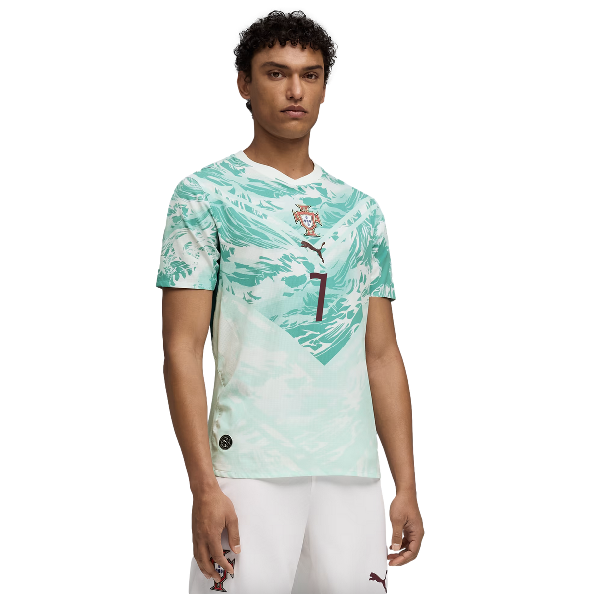 A young man models a white and light green abstract-patterned soccer jersey with a central crest and the number 7, paired with white shorts, against a black background.