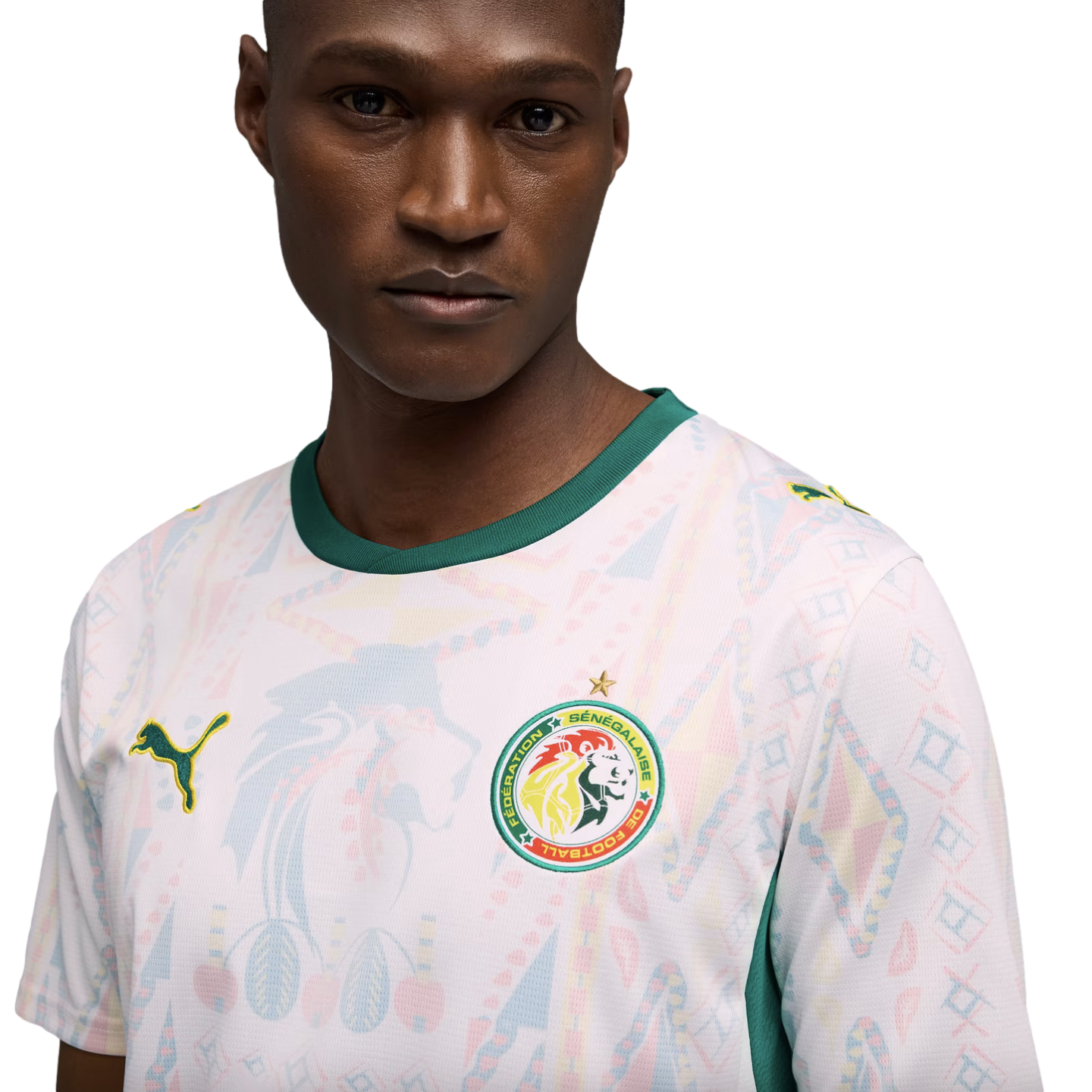 A man in a white Senegal national team soccer jersey with green trim and faint colorful geometric patterns, set against a solid black background.