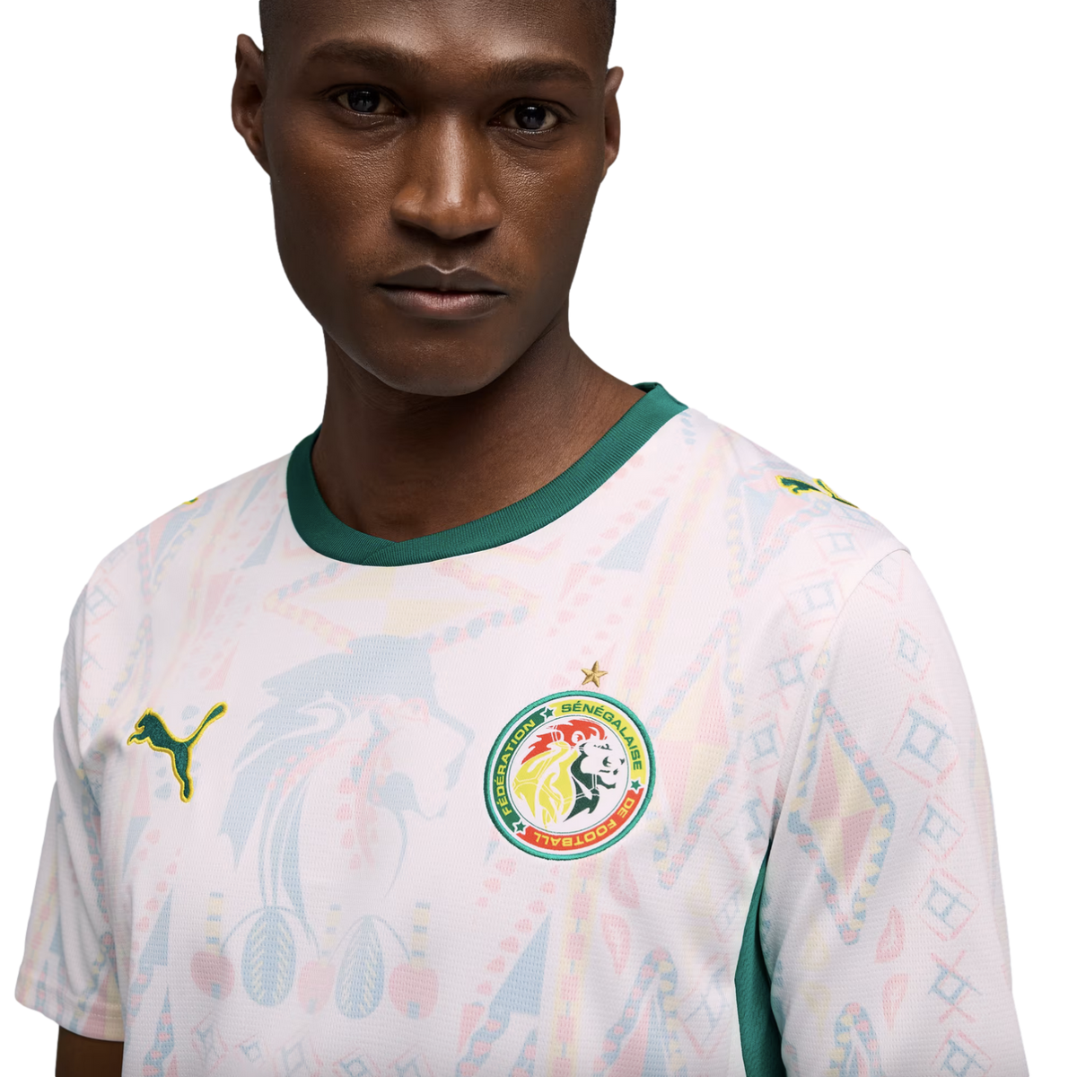 A man in a white Senegal national team soccer jersey with green trim and faint colorful geometric patterns, set against a solid black background.