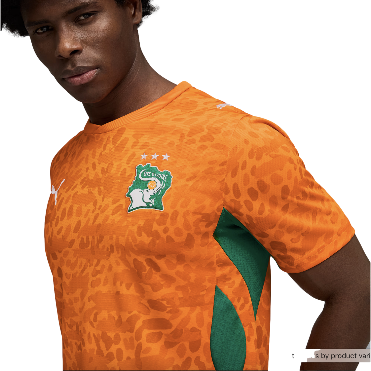 A close-up of a man wearing an orange Côte d'Ivoire national football team jersey against a black background. The jersey features a tonal animal-print pattern, green mesh panels on the sides, and the team's crest on the chest, which includes a white eleph