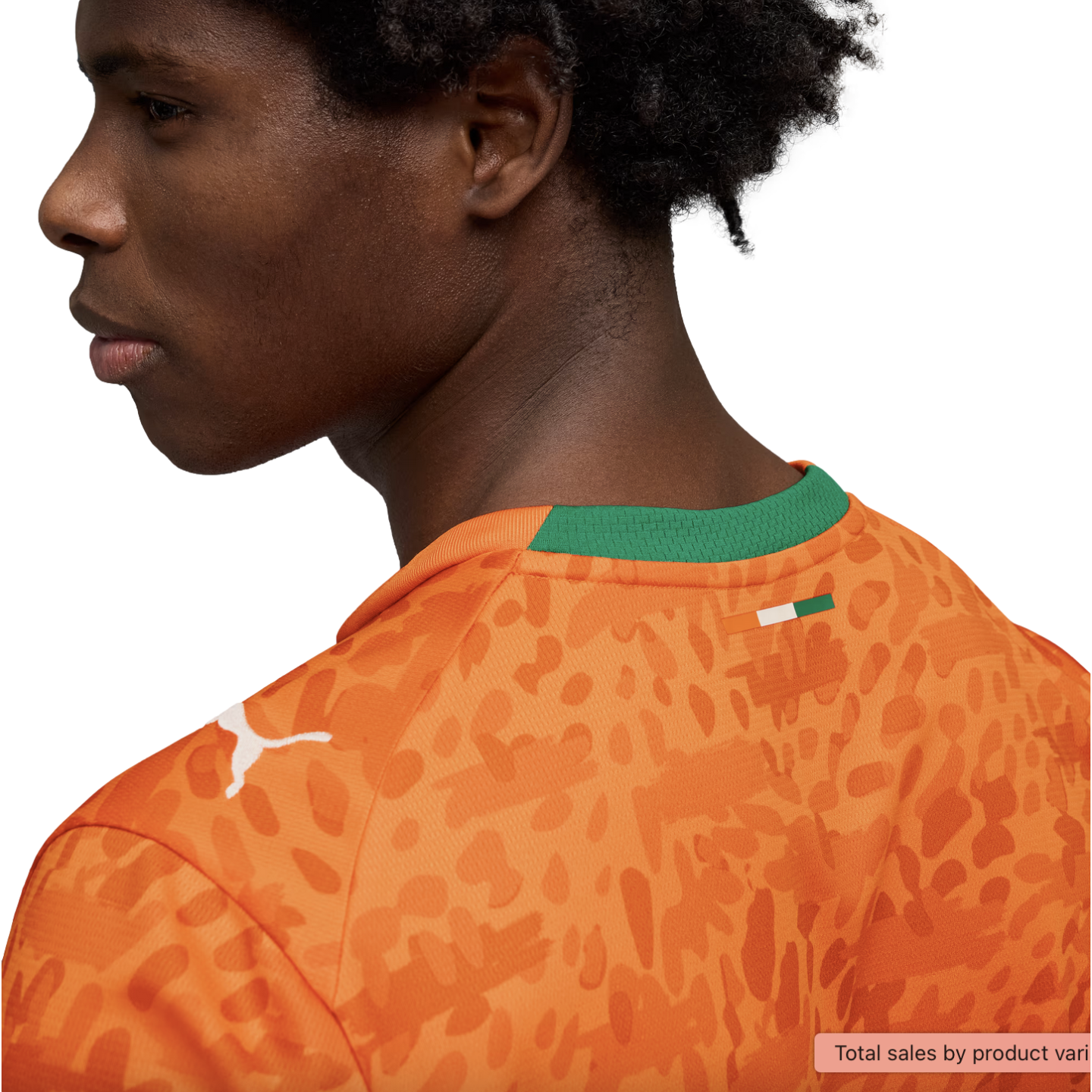 A profile view of a young man with dark curly hair wearing an orange Puma jersey against a black background. The jersey features a tonal abstract animal print, a white Puma logo on the shoulder, and a green collar with a small flag of the Ivory Coast on t