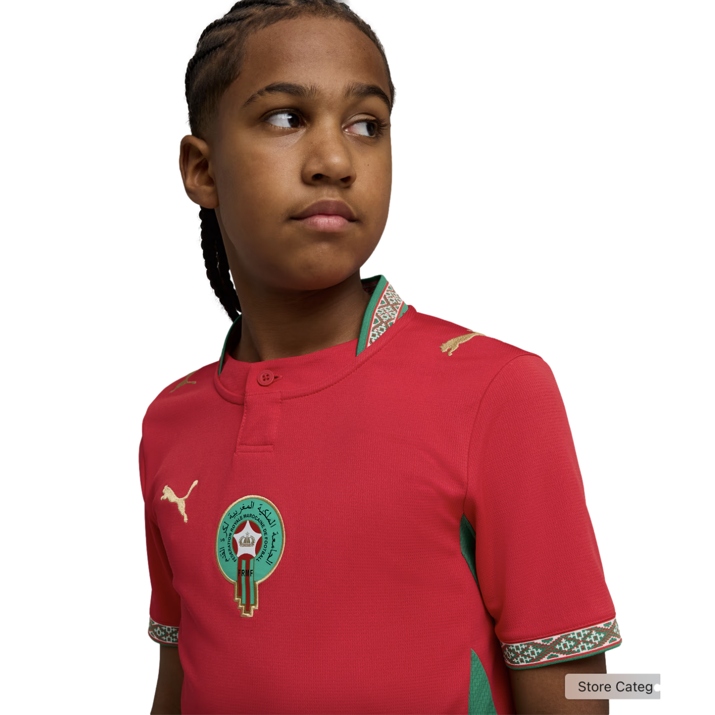 A young person with braided hair looking to the side, wearing a red Morocco national football team jersey by Puma, against a solid black background.