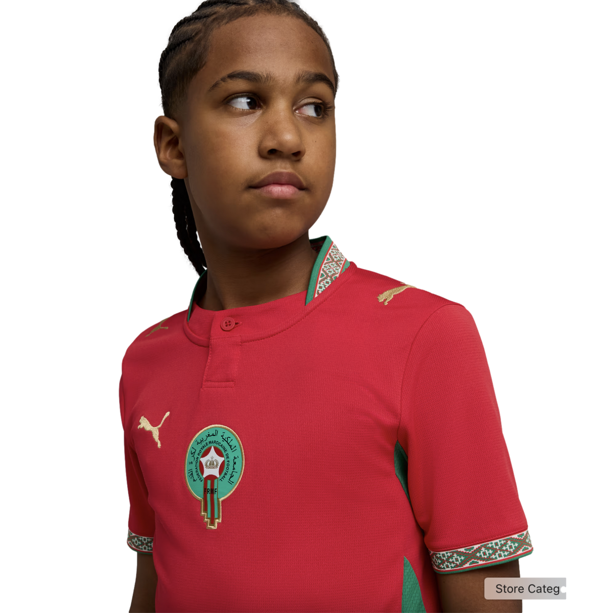 A young person with braided hair looking to the side, wearing a red Morocco national football team jersey by Puma, against a solid black background.