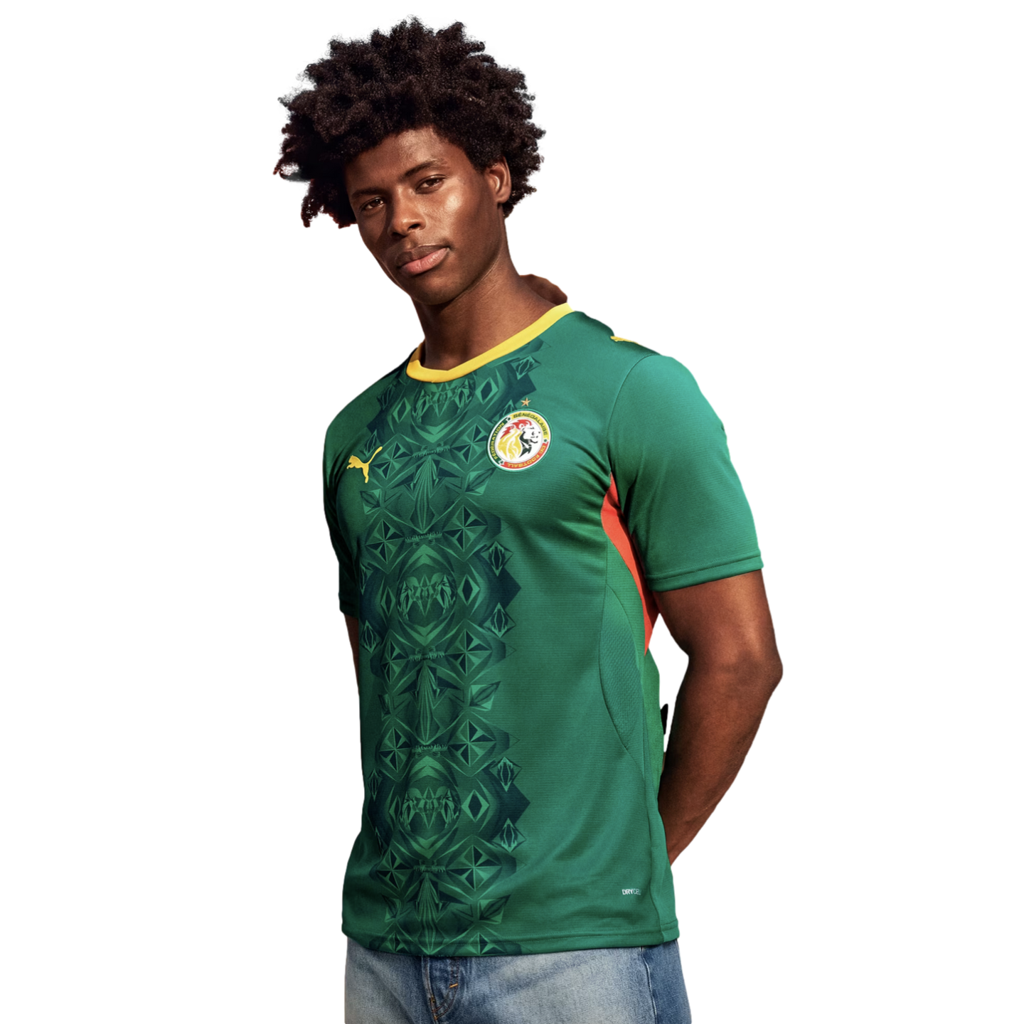 A man with dark, curly hair poses in a green Senegal national team soccer jersey against a solid black background. The jersey features a yellow collar, a dark green geometric pattern down the center, the Puma logo, and the national team crest. He is weari