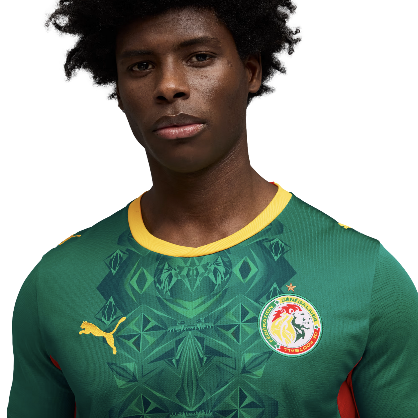 A close-up portrait of a Black man with afro-textured hair wearing a green Puma Senegal national football team jersey with intricate geometric patterns, looking directly at the camera against a black background.