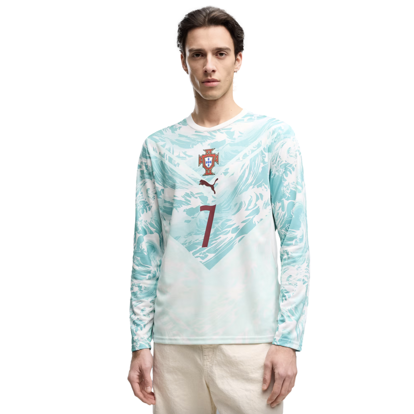 A young man stands against a black background wearing a light blue and white wavy-patterned long-sleeved shirt. The shirt features the Portugal national team crest, a brown Puma logo, and a large brown number 7 on the front.