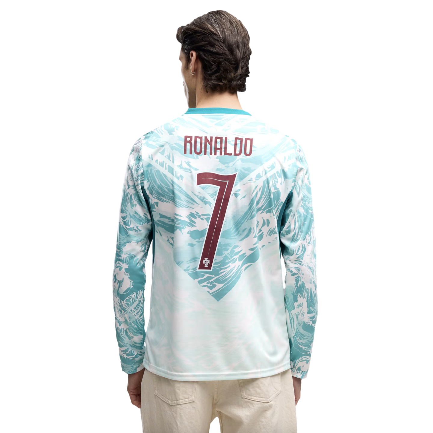 Rear view of a man wearing a long-sleeved teal and white jersey featuring a wavy, ocean-inspired graphic. The name "RONALDO" and the number "7" are printed on the back in maroon. He is also wearing light-colored trousers against a solid black background.