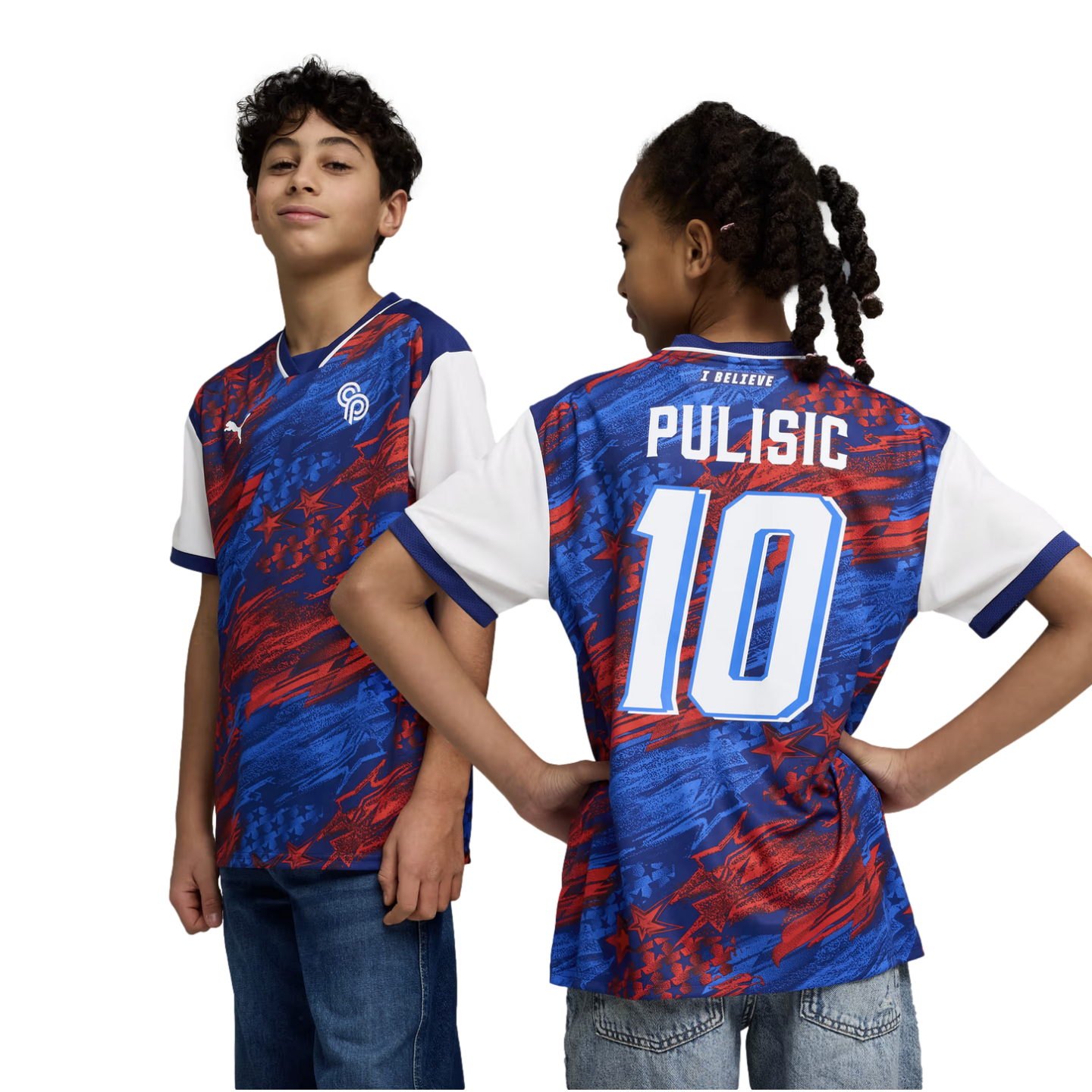 A studio portrait against a black background shows two young children modeling a blue and red Puma soccer jersey. The boy on the left faces forward, showing the front of the jersey with its abstract star pattern and Puma logo. The girl on the right faces