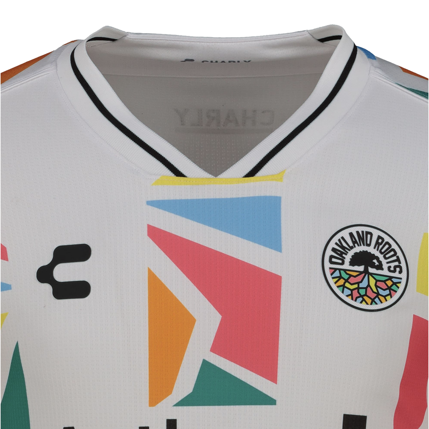 Close-up of a white Oakland Roots SC soccer jersey by Charly, featuring a large, colorful geometric pattern on the chest and the team's circular tree crest.