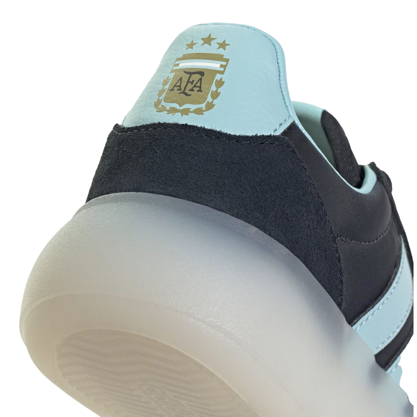 A close-up shot focusing on the heel of an Adidas shoe, featuring a light blue panel with the gold Argentina Football Association (AFA) crest and three stars. Below the blue panel is a dark navy textured material and a thick, semi-translucent white sole,